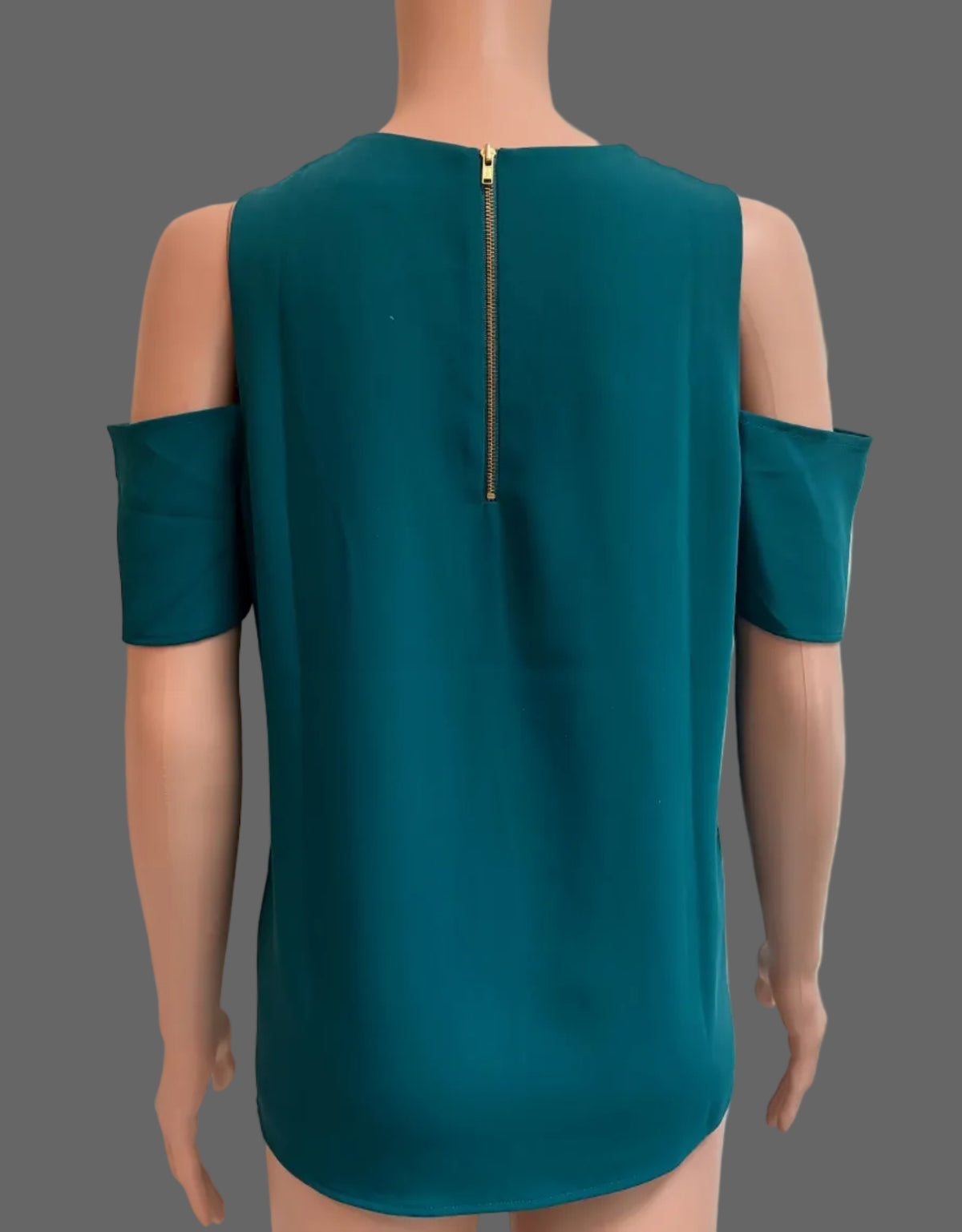 A teal cold-shoulder top with a gold zipper at the back, displayed on a mannequin in front of a white paneled door.