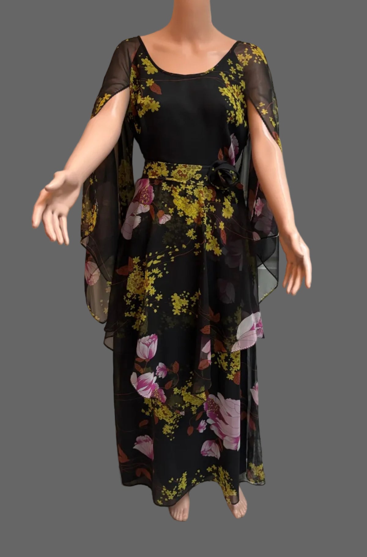 A black maxi dress with a yellow and pink floral print displayed on a mannequin in front of a white paneled door.