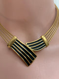 A gold-toned multi-strand collar necklace with black enamel inlay, displayed on a pink mannequin bust.
