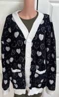 A black fuzzy cardigan sweater with white trim and a repeating pattern of white hearts, peace signs, and smiley faces, displayed on a mannequin torso.