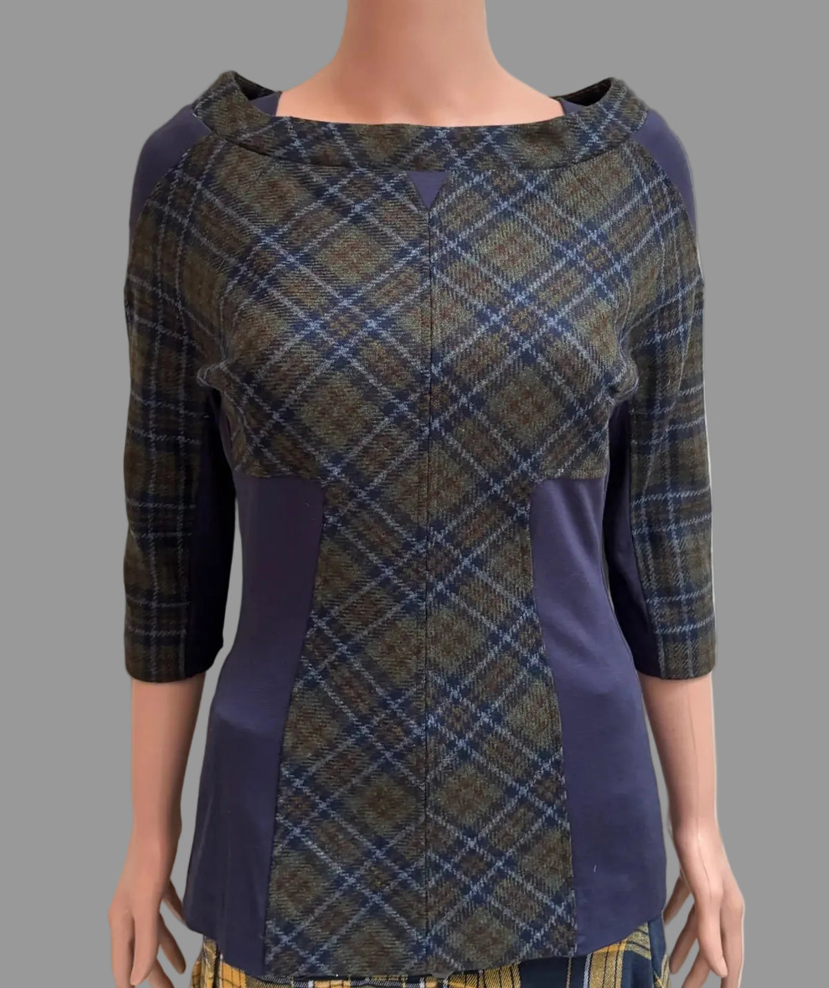 A women's three-quarter sleeve top displayed on a mannequin torso, featuring a blue and brown plaid pattern with solid navy blue side panels and a boat neckline, paired with a matching plaid skirt in front of a white paneled door.