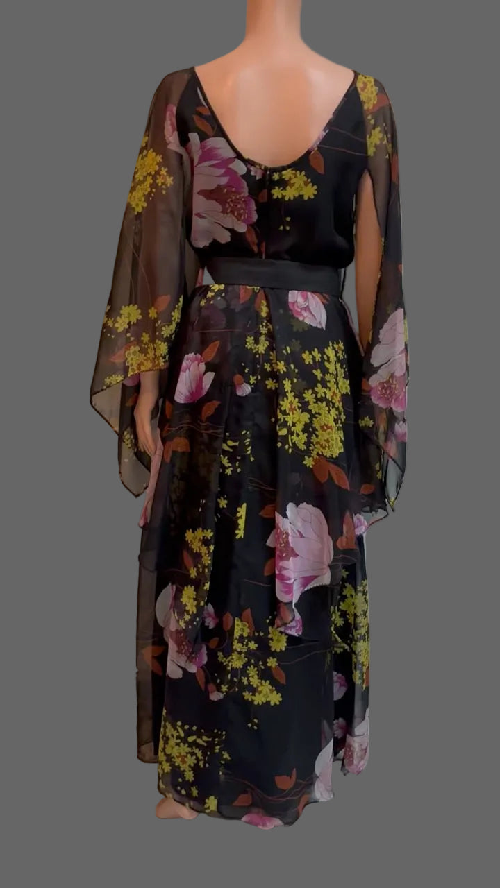 A black maxi dress with a pink and yellow floral print, displayed on a mannequin in front of a white paneled door.