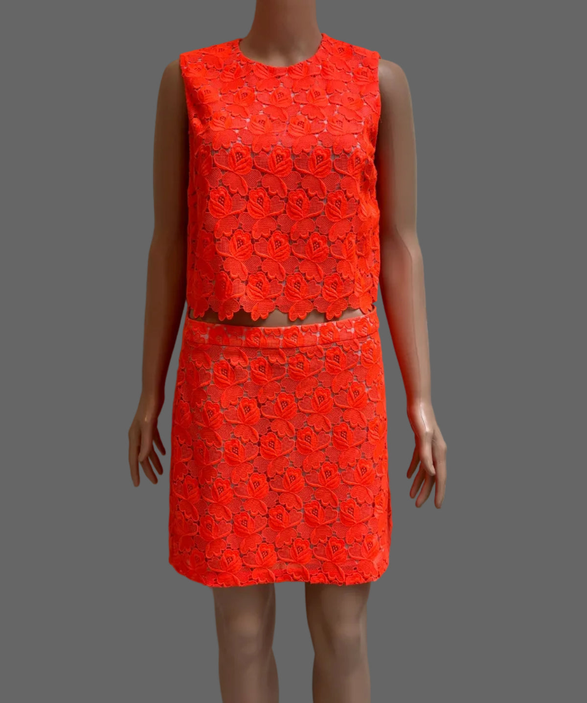 A sleeveless bright orange-red textured dress displayed on a mannequin in front of a white paneled door.