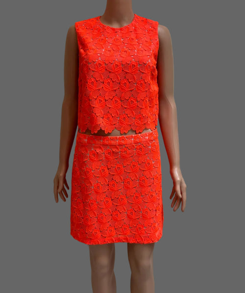 A sleeveless bright orange-red textured dress displayed on a mannequin in front of a white paneled door.