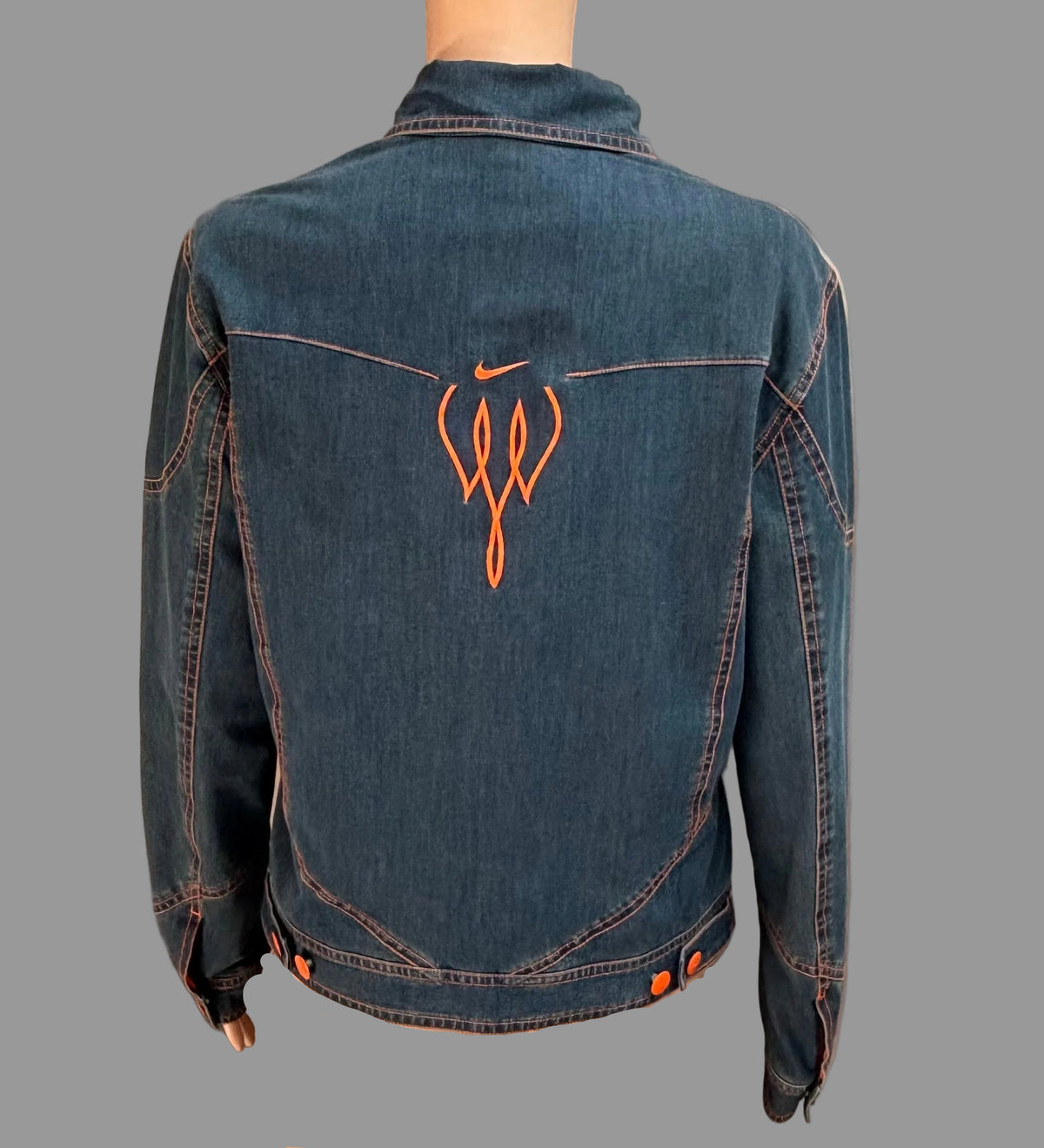 Blue denim jacket with orange logo on a mannequin against a beige curtain background