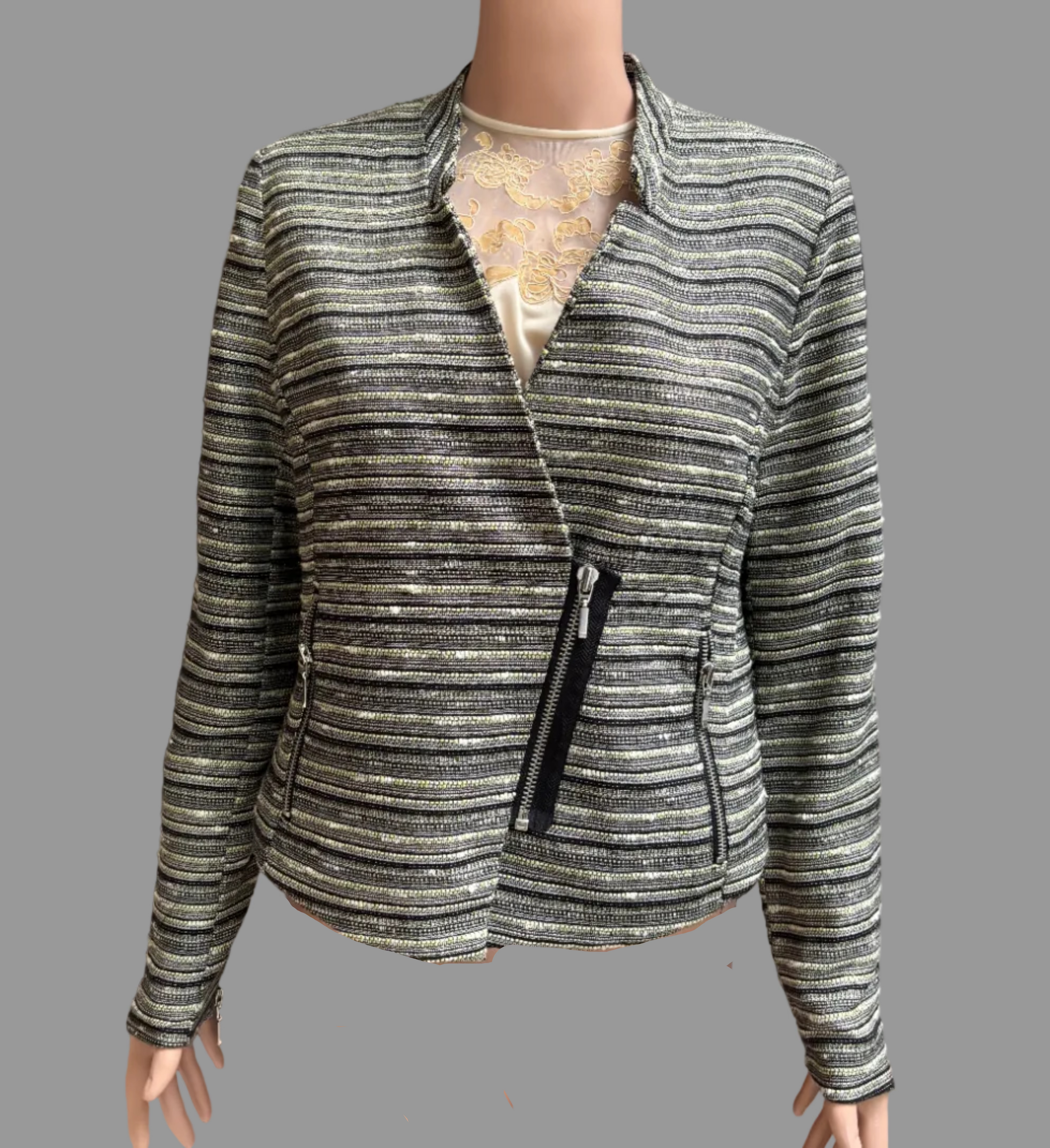 A women's zip-front jacket with horizontal metallic stripes in silver, gray, and black, displayed on a mannequin torso in front of brown curtains.