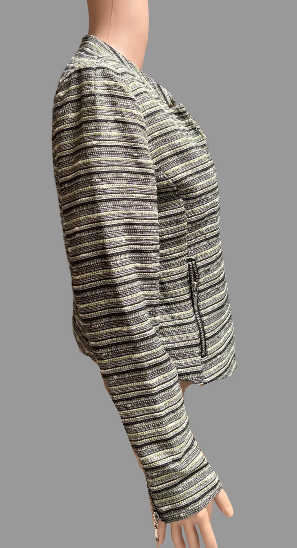 A cropped, long-sleeve jacket with horizontal metallic stripes in silver, black, and gold, displayed on a mannequin torso in front of a brown curtain.