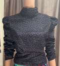 A navy blue, long-sleeve mock neck top with white polka dots and puffed sleeves. Open in the back