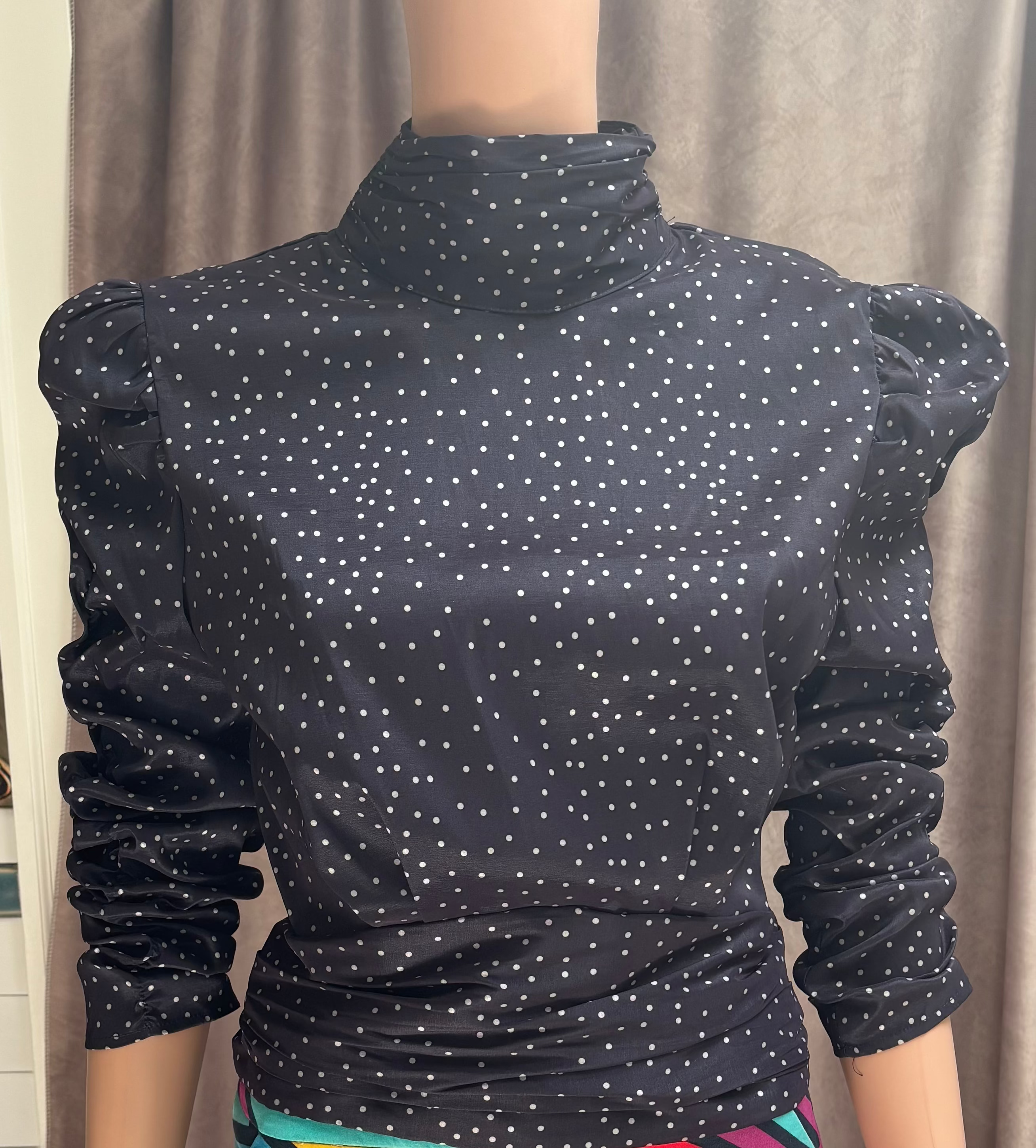 A navy blue, long-sleeve mock neck top with white polka dots and puffed sleeves. Open in the back