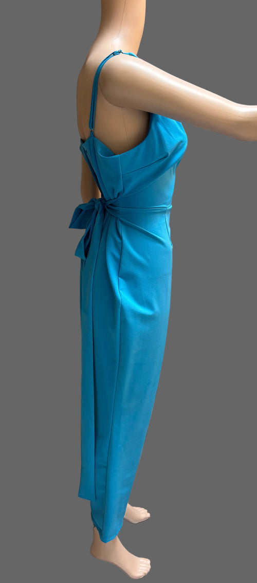 A bright blue sleeveless maxi dress with thin straps, a back tie detail, and a draped waist, displayed on a mannequin in front of brown curtains.