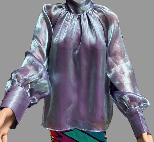 A sheer, iridescent lavender-purple blouse with a high gathered neckline and voluminous balloon sleeves, shown on a mannequin or person against brown curtains.